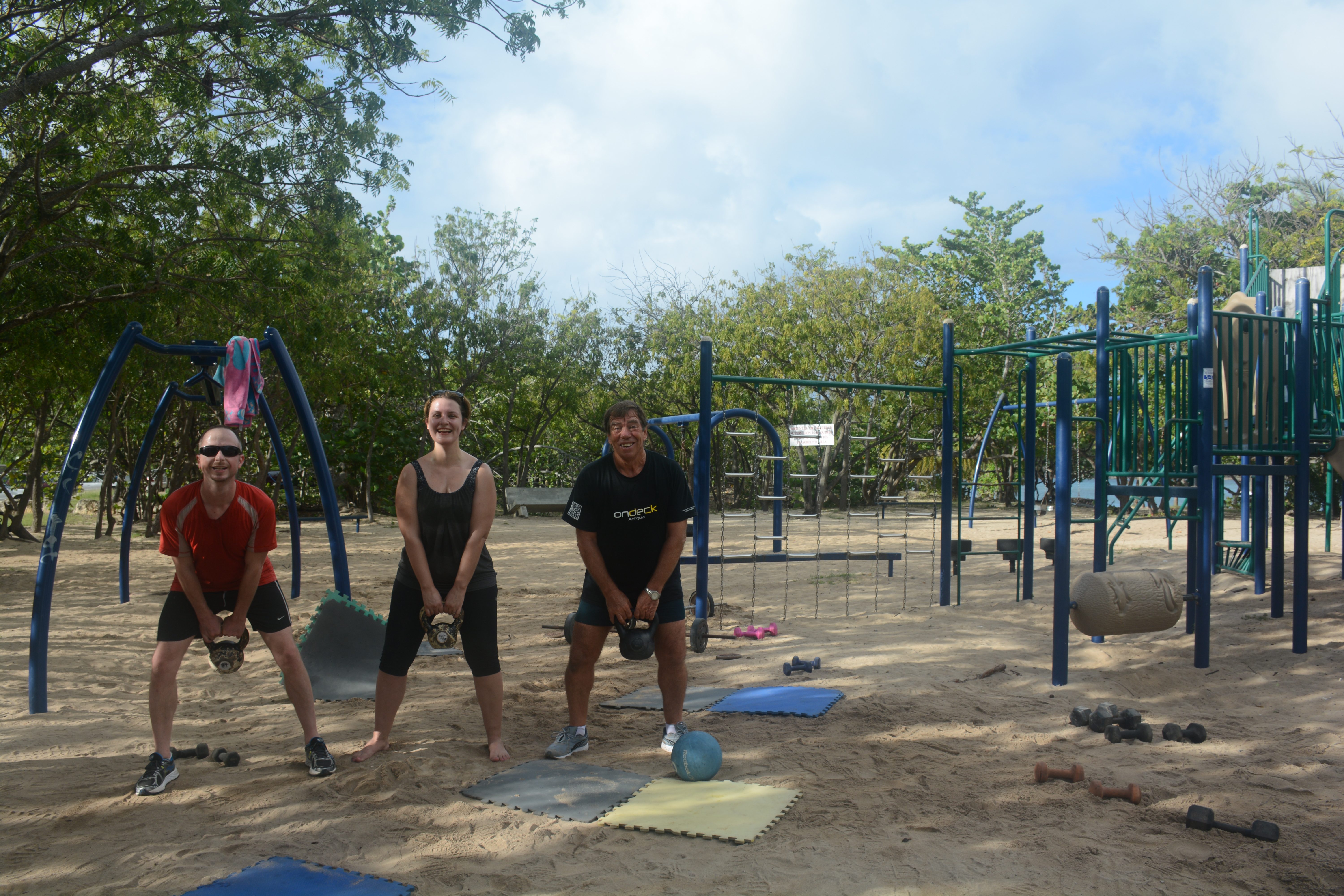 Three people on a beach with kettlebells.